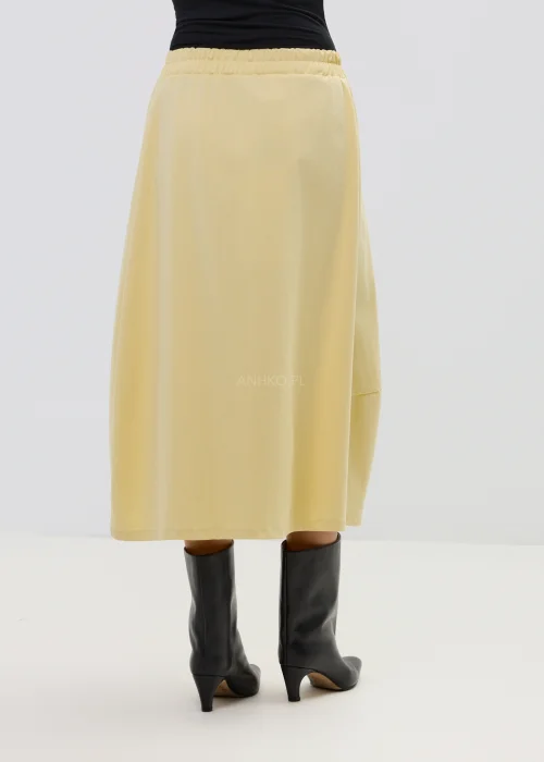 Żółta spódnica midi o asymetrycznym kroju z ozdobnymi czarnymi guzikami i elastyczną talią, elegancka i nowoczesna w stylizacji z wysokimi botkami.