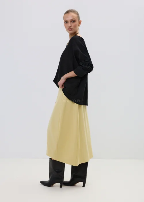 Żółta spódnica midi o asymetrycznym kroju z ozdobnymi czarnymi guzikami i elastyczną talią, elegancka i nowoczesna w stylizacji z wysokimi botkami.