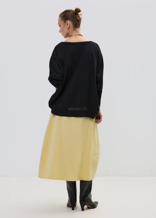 Żółta spódnica midi o asymetrycznym kroju z ozdobnymi czarnymi guzikami i elastyczną talią, elegancka i nowoczesna w stylizacji z wysokimi botkami.