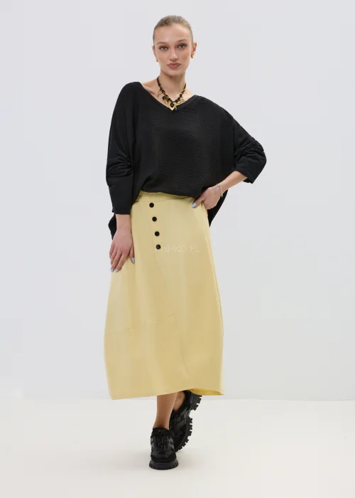 Żółta spódnica midi o asymetrycznym kroju z ozdobnymi czarnymi guzikami i elastyczną talią, elegancka i nowoczesna w stylizacji z wysokimi botkami.
