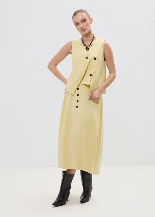 Żółta spódnica midi o asymetrycznym kroju z ozdobnymi czarnymi guzikami i elastyczną talią, elegancka i nowoczesna w stylizacji z wysokimi botkami.