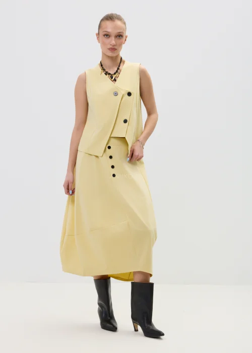 Żółta kamizelka damska o kopertowym kroju z ozdobnymi czarnymi guzikami, elegancka i nowoczesna, w stylizacji z dopasowaną spódnicą.