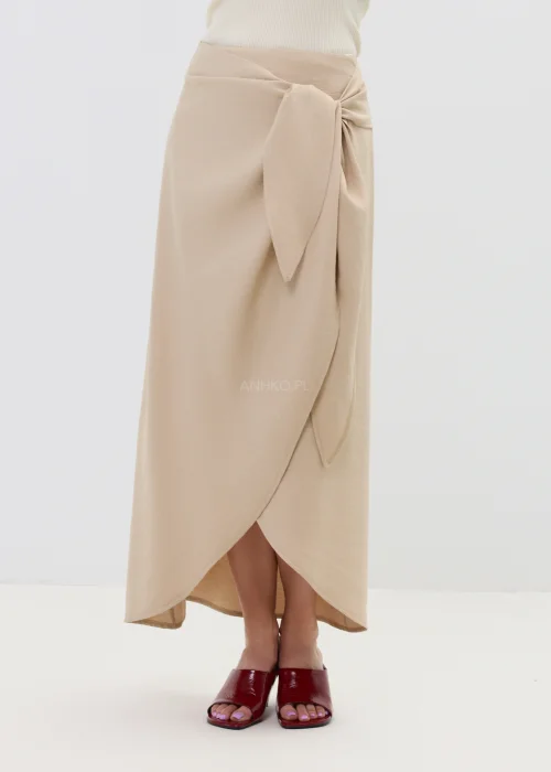 Beżowa spódnica z kopertowym wiązaniem w talii, o płynnie układającym się fasonie, elegancka i minimalistyczna w stylizacji z sandałami na obcasie.