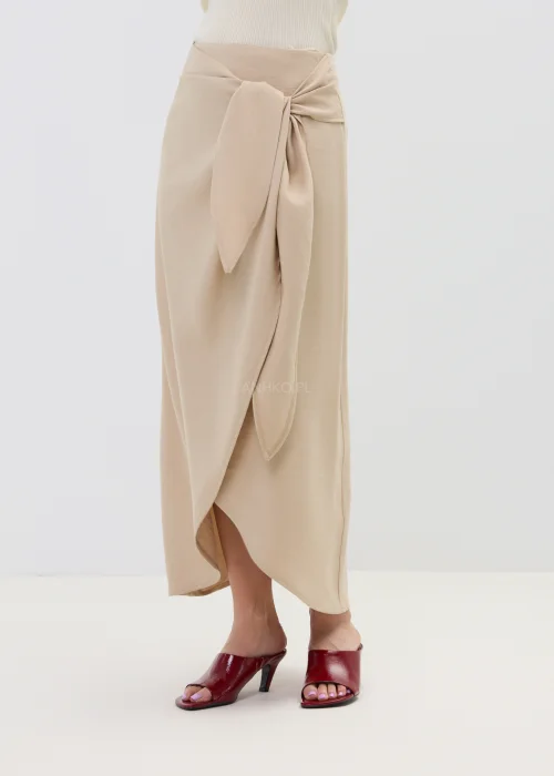Beżowa spódnica z kopertowym wiązaniem w talii, o płynnie układającym się fasonie, elegancka i minimalistyczna w stylizacji z sandałami na obcasie.