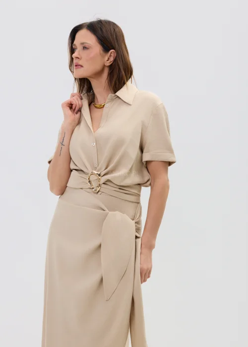 Beżowa bluzka damska z krótkim rękawem i ozdobnym wiązaniem z klamrą, lekka i elegancka.