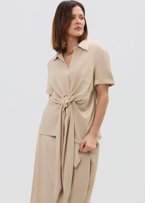 Beżowa bluzka damska z krótkim rękawem i ozdobnym wiązaniem z klamrą, lekka i elegancka.