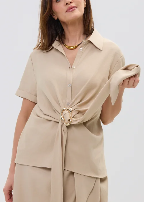 Beżowa bluzka damska z krótkim rękawem i ozdobnym wiązaniem z klamrą, lekka i elegancka.