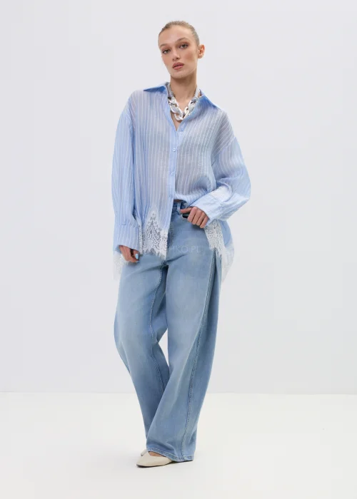 Niebieska koszula damska w delikatne paski z koronkowym wykończeniem u dołu, lekko transparentna, o luźnym kroju w stylizacji casual z jeansami.