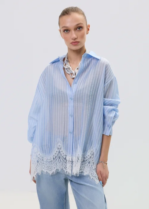 Niebieska koszula damska w delikatne paski z koronkowym wykończeniem u dołu, lekko transparentna, o luźnym kroju w stylizacji casual z jeansami.