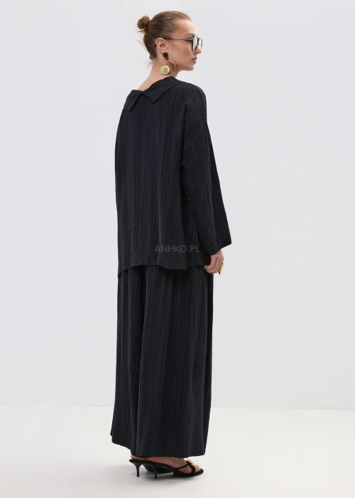 Czarna bluzka damska w delikatny prążek z luźnym krojem i szerokim dekoltem typu komin, w eleganckiej stylizacji z biżuterią.