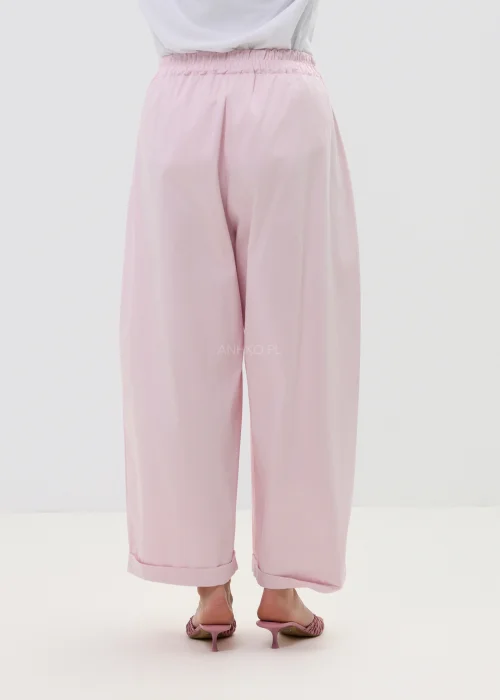 Różowe spodnie damskie z szerokimi nogawkami i podwiniętym dołem, luźny fason, elegancko-casualowa stylizacja.