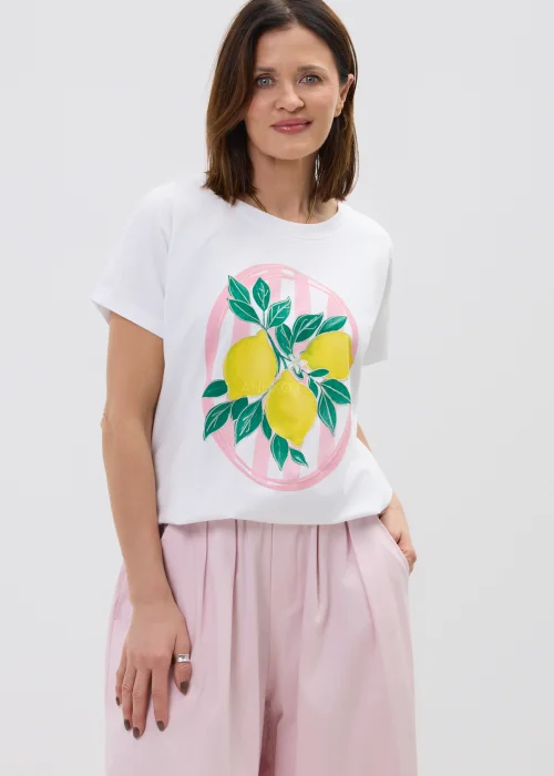 Biały t-shirt damski z nadrukiem cytryn i zielonych liści, o luźnym kroju, stylizowany z różowymi spodniami w casualowym looku.