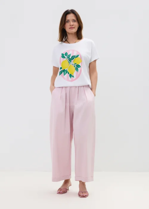 Biały t-shirt damski z nadrukiem cytryn i zielonych liści, o luźnym kroju, stylizowany z różowymi spodniami w casualowym looku.