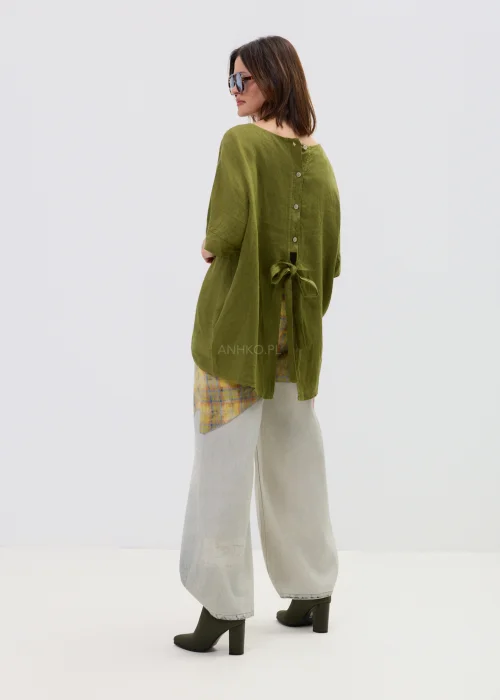 Lniana bluzka oversize w kolorze oliwkowej zieleni z krótkim rękawem i wiązaniem oraz guzikami na plecach, o luźnym kroju, stylizowana z jasnymi spodniami.