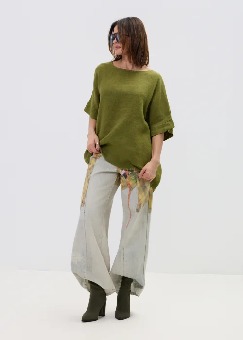 Lniana bluzka oversize w kolorze oliwkowej zieleni z krótkim rękawem i wiązaniem oraz guzikami na plecach, o luźnym kroju, stylizowana z jasnymi spodniami.