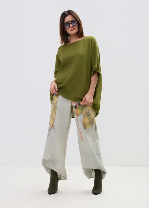 Lniana bluzka oversize w kolorze oliwkowej zieleni z krótkim rękawem i wiązaniem oraz guzikami na plecach, o luźnym kroju, stylizowana z jasnymi spodniami.