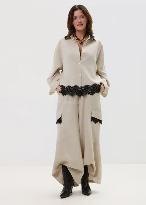 Koszula oversize w kolorze beżowym z czarną koronką przy kołnierzu i dole, o luźnym kroju z długim rękawem, stylizowana w elegancko-nowoczesnym zestawie.