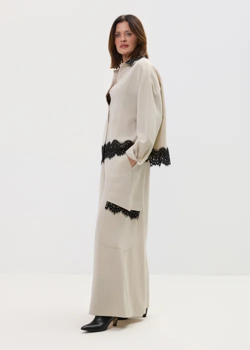 Koszula oversize w kolorze beżowym z czarną koronką przy kołnierzu i dole, o luźnym kroju z długim rękawem, stylizowana w elegancko-nowoczesnym zestawie.
