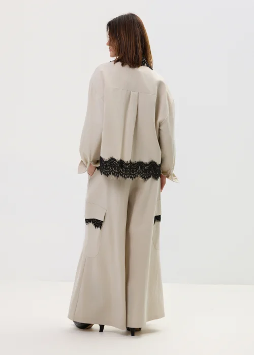 Koszula oversize w kolorze beżowym z czarną koronką przy kołnierzu i dole, o luźnym kroju z długim rękawem, stylizowana w elegancko-nowoczesnym zestawie.