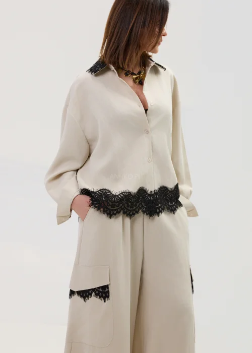 Koszula oversize w kolorze beżowym z czarną koronką przy kołnierzu i dole, o luźnym kroju z długim rękawem, stylizowana w elegancko-nowoczesnym zestawie.