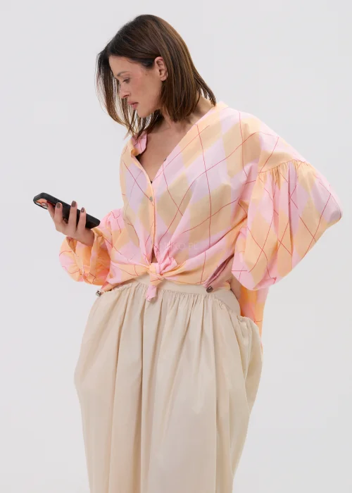 Koszula oversize w pastelową kratę w odcieniach różu i pomarańczu, z bufiastymi rękawami i wiązaniem z przodu, stylizowana z długą beżową spódnicą w kobiecym, lekkim looku.