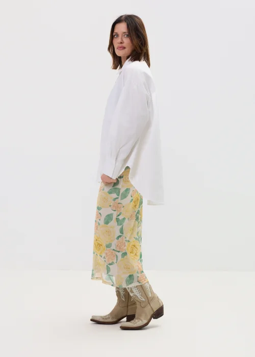 Koszula oversize w kolorze białym z ozdobnymi biżuteryjnymi guzikami w formie kwiatów, o luźnym kroju z szerokimi rękawami, stylizowana z kwiatową spódnicą.