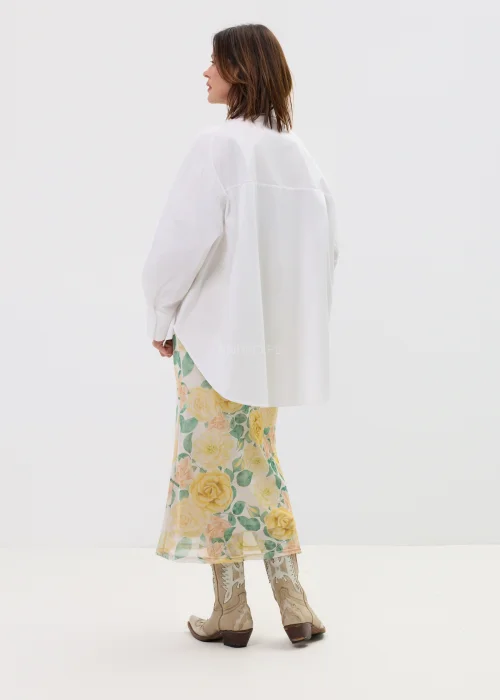 Koszula oversize w kolorze białym z ozdobnymi biżuteryjnymi guzikami w formie kwiatów, o luźnym kroju z szerokimi rękawami, stylizowana z kwiatową spódnicą.