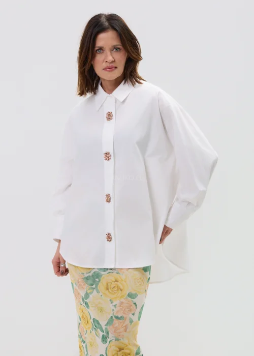 Koszula oversize w kolorze białym z ozdobnymi biżuteryjnymi guzikami w formie kwiatów, o luźnym kroju z szerokimi rękawami, stylizowana z kwiatową spódnicą.