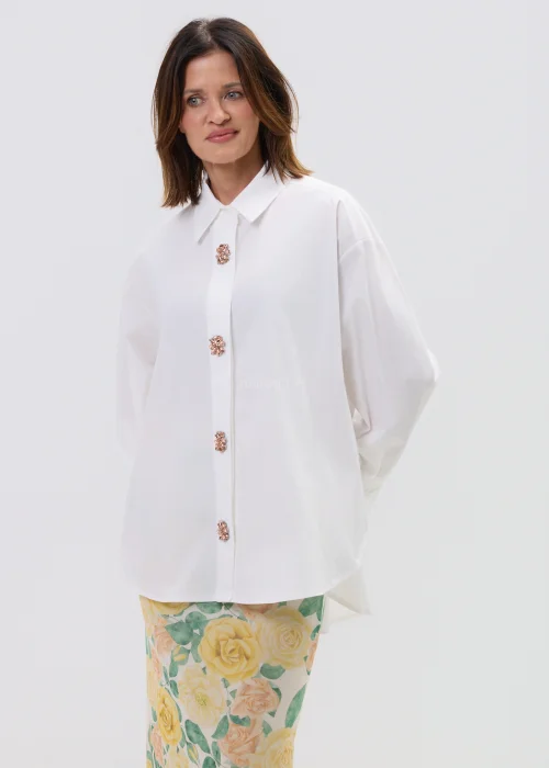 Koszula oversize w kolorze białym z ozdobnymi biżuteryjnymi guzikami w formie kwiatów, o luźnym kroju z szerokimi rękawami, stylizowana z kwiatową spódnicą.