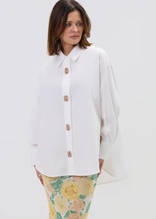 Koszula oversize w kolorze białym z ozdobnymi biżuteryjnymi guzikami w formie kwiatów, o luźnym kroju z szerokimi rękawami, stylizowana z kwiatową spódnicą.