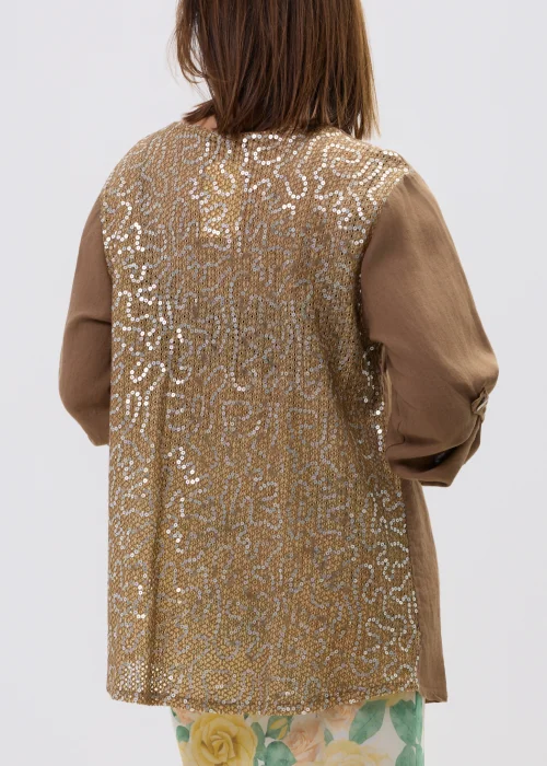 Lniana koszula oversize w kolorze brązowym z cekinowymi zdobieniami i kieszeniami, z długim rękawem i zapięciem na guziki, stylizowana z kwiatową spódnicą.