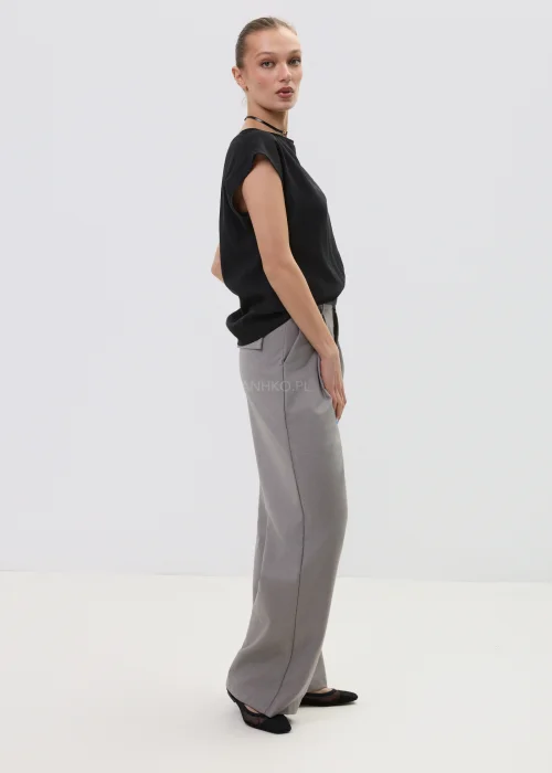 Czarna bluzka damska bez rękawów z luźnym krojem i ozdobnym zapięciem na ramieniu, elegancka minimalistyczna stylizacja.