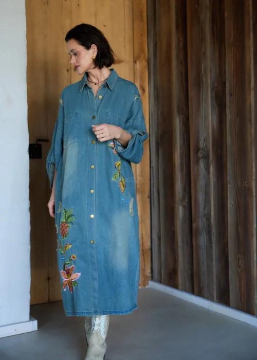 Sukienka koszulowa midi z denimu w odcieniu niebieskim, z haftowanymi kwiatami i przetarciami, o luźnym kroju oversize, stylizowana z kozakami w casualowym wydaniu.