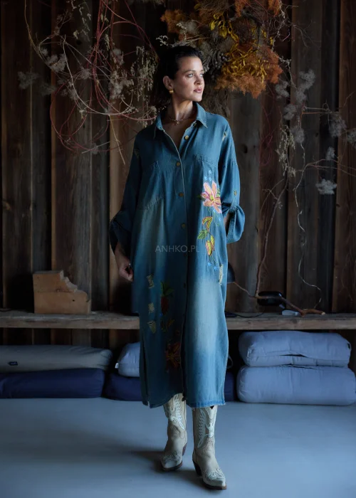 Sukienka koszulowa midi z denimu w odcieniu niebieskim, z haftowanymi kwiatami i przetarciami, o luźnym kroju oversize, stylizowana z kozakami w casualowym wydaniu.