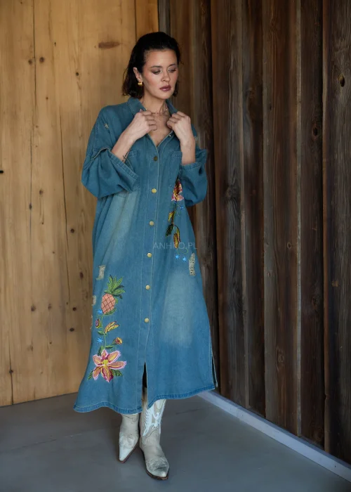 Sukienka koszulowa midi z denimu w odcieniu niebieskim, z haftowanymi kwiatami i przetarciami, o luźnym kroju oversize, stylizowana z kozakami w casualowym wydaniu.