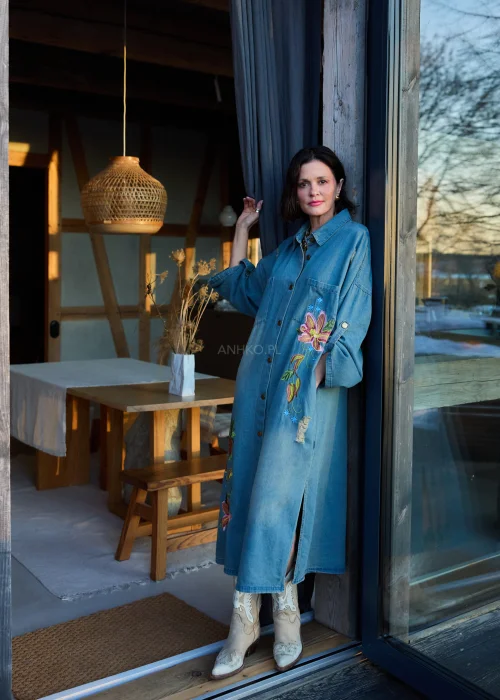 Sukienka koszulowa midi z denimu w odcieniu niebieskim, z haftowanymi kwiatami i przetarciami, o luźnym kroju oversize, stylizowana z kozakami w casualowym wydaniu.