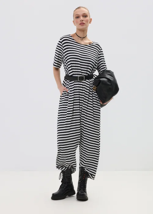 Kombinezon damski w czarno-białe paski o luźnym kroju z obniżonym krokiem, przewiązany paskiem w talii, stylizowany z ciężkimi botkami.