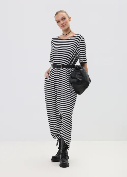 Kombinezon damski w czarno-białe paski o luźnym kroju z obniżonym krokiem, przewiązany paskiem w talii, stylizowany z ciężkimi botkami.