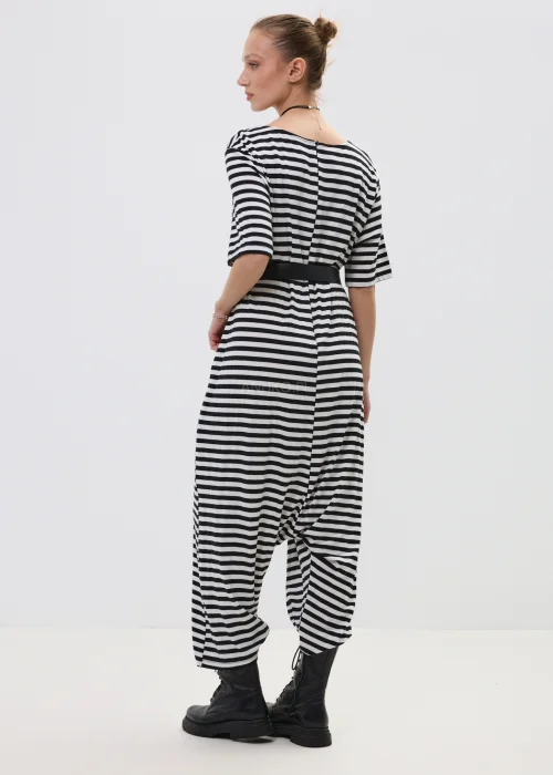 Kombinezon damski w czarno-białe paski o luźnym kroju z obniżonym krokiem, przewiązany paskiem w talii, stylizowany z ciężkimi botkami.