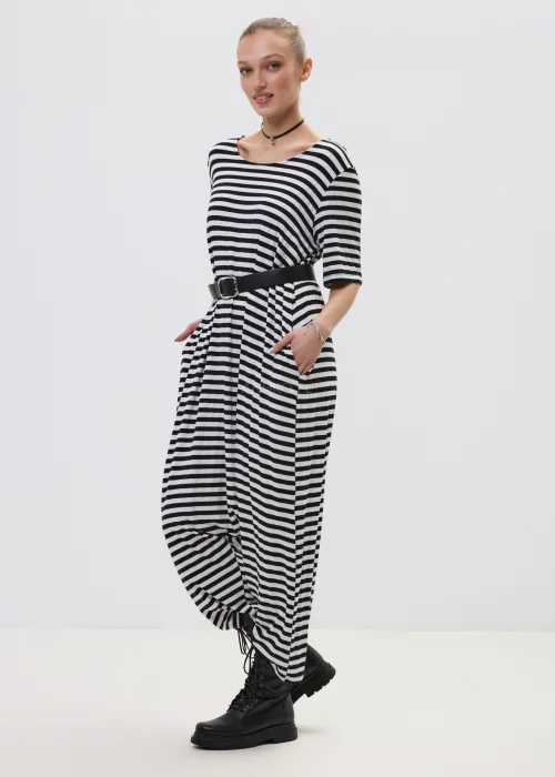 Kombinezon damski w czarno-białe paski o luźnym kroju z obniżonym krokiem, przewiązany paskiem w talii, stylizowany z ciężkimi botkami.