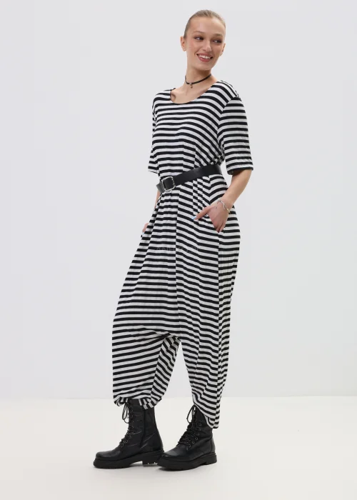 Kombinezon damski w czarno-białe paski o luźnym kroju z obniżonym krokiem, przewiązany paskiem w talii, stylizowany z ciężkimi botkami.