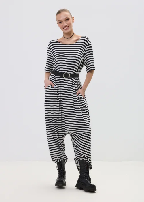 Kombinezon damski w czarno-białe paski o luźnym kroju z obniżonym krokiem, przewiązany paskiem w talii, stylizowany z ciężkimi botkami.