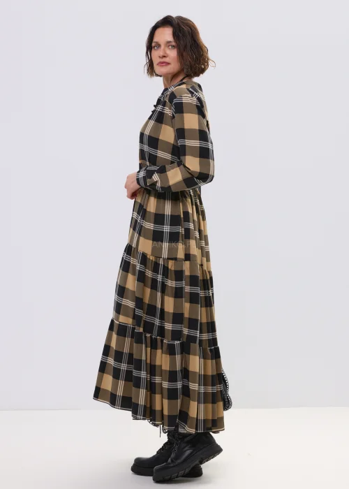 Sukienka maxi w beżowo-czarną kratę z paskiem w talii, o luźnym kroju i warstwowym dole, stylizowana z ciężkimi botkami i dużą torebką.