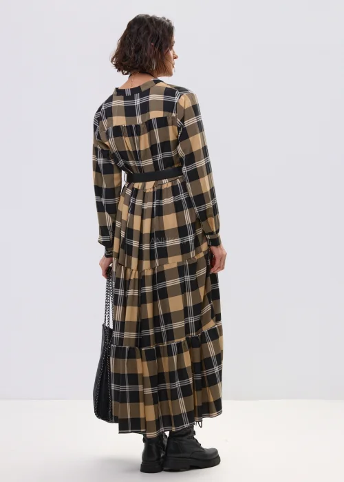 Sukienka maxi w beżowo-czarną kratę z paskiem w talii, o luźnym kroju i warstwowym dole, stylizowana z ciężkimi botkami i dużą torebką.