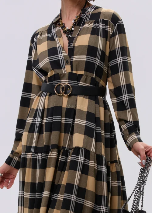 Sukienka maxi w beżowo-czarną kratę z paskiem w talii, o luźnym kroju i warstwowym dole, stylizowana z ciężkimi botkami i dużą torebką.