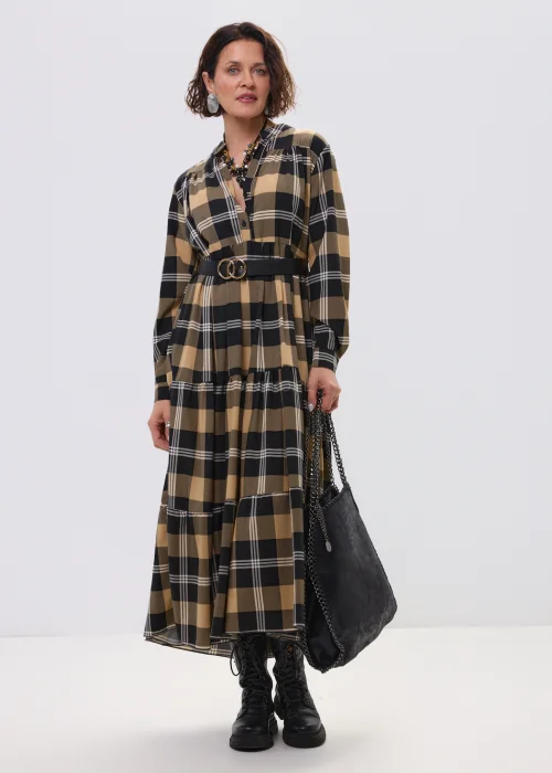 Sukienka maxi w beżowo-czarną kratę z paskiem w talii, o luźnym kroju i warstwowym dole, stylizowana z ciężkimi botkami i dużą torebką.