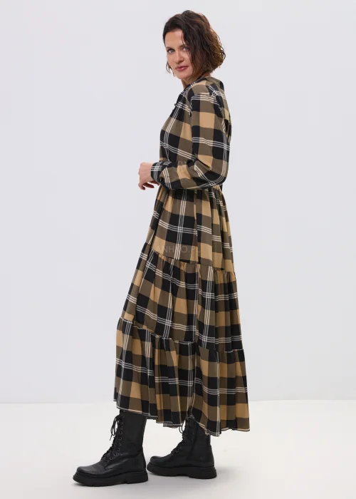 Sukienka maxi w beżowo-czarną kratę z paskiem w talii, o luźnym kroju i warstwowym dole, stylizowana z ciężkimi botkami i dużą torebką.
