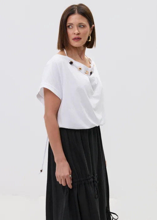 Biała bluzka o luźnym kroju z krótkim rękawem, z ozdobnym dekoltem wykończonym koralikami, stylizowana z czarną spódnicą w minimalistycznym, eleganckim wydaniu.