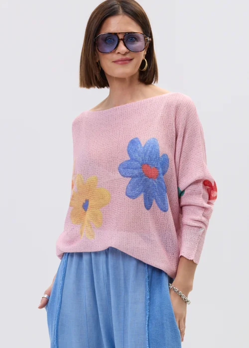 Pudrowo różowy sweter o lekkim, luźnym splocie z kolorowym motywem kwiatów, zestawiony z niebieską spódnicą w casualowej stylizacji.