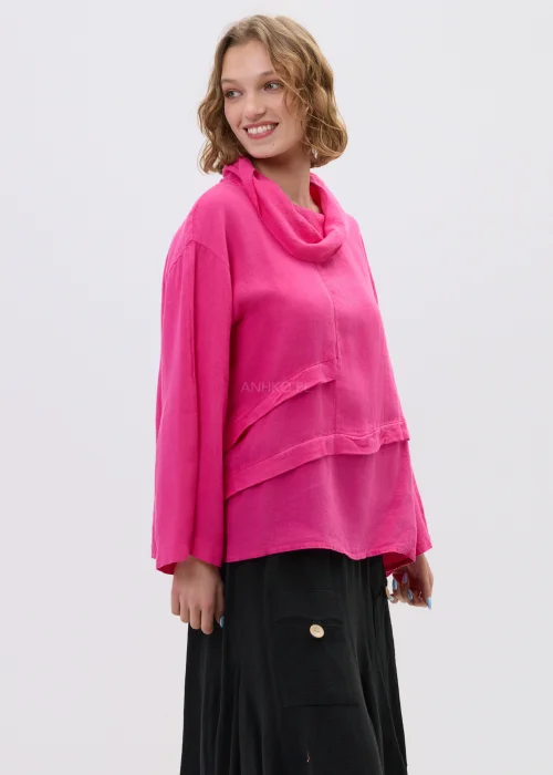 Lniana bluzka damska w kolorze magenta o oversize’owym kroju z kominowym dekoltem i asymetrycznym dołem, stylizowana z czarną spódnicą.